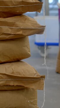 tight vertical shot showing stacked brown kraft sacks on wooden pallet inside industrial bakery or storage area, sacks display folded serrated edges, creases, with