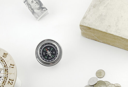 A magnetic compass, paper money and coins, a book, and a watch. Light background