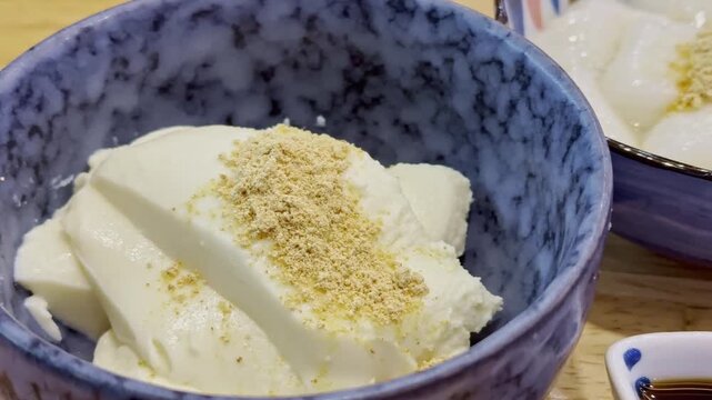 Close-up of soft white shiratama dango topped with fragrant kinako powder and sweet syrup, served in a decorative ceramic bowl as a traditional Japanese dessert.