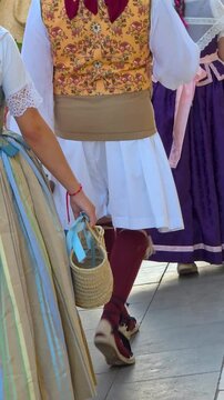 Rear low angle slow motion shot of people dressed in authentic Valencian traditional folk costumes carrying straw baskets during grape harvest parade in Spain.
