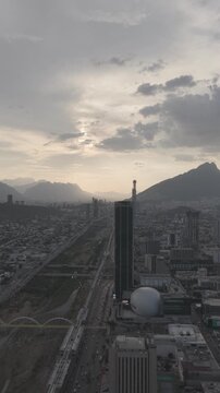 Aerial lateral view over downtown Monterrey toward the Avenida Constituci&oacute;n skyline and mountains during golden hour, Nuevo Le&oacute;n. Vertical video. D-Log M