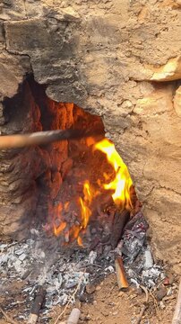 Slow motion shot of stoking roaring fire with poker tool in traditional stone furnace during Escalda raisin festival in Spain.