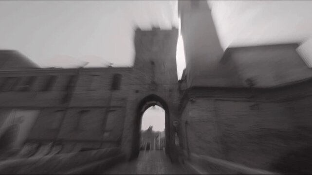 Scorcio suggestivo in bianco e nero di un castello medievale, con un'antica porta ad arco e torri storiche sotto un cielo coperto