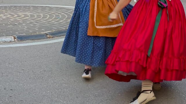 Low angle close up slow motion shot of women dancing in vibrant red and blue traditional Valencian folk dresses with espadrilles during harvest festival in Spain.