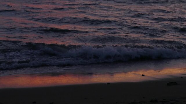 Pacific Ocean waves on the beach shoreline during a beautiful sunset in Maalaea Bay from Kihei, Maui, Hawaii. The colors, clouds and lingering gold and red sunlight reflected in the water and wet sand