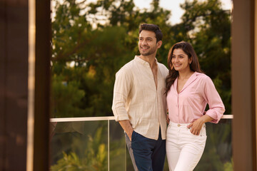 Obraz premium Happy Young Indian Couple Standing in Lavish Posh Glass Balcony as Proud Real Estate Property Owner