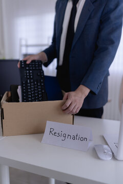 Asian businessman in formal suit packing cardboard box with office belongings after job resignation with copy space