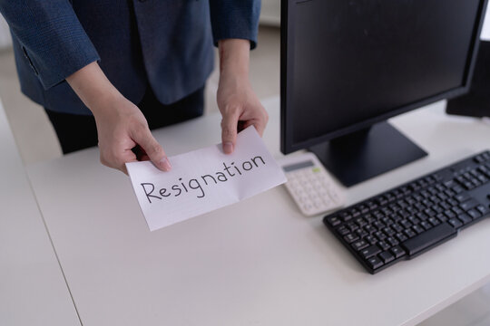Asian businesswoman placing handwritten resignation letter on office desk near computer with copy space
