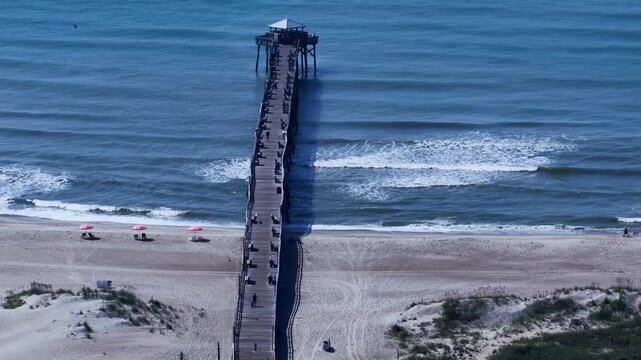 Atlantic Beach, NC Fishing pier with gentle breaking ocean waves and people on beach on sunny day
