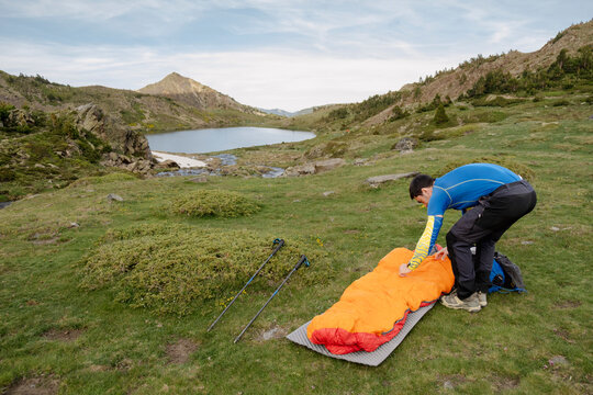 UGC Man setting up sleeping bag by alpine lake in Pyrenees