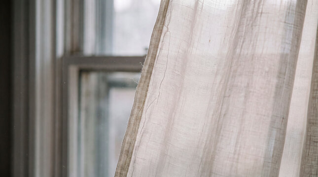Sheer linen curtain sways gently by window evoking calm minimalist stillness