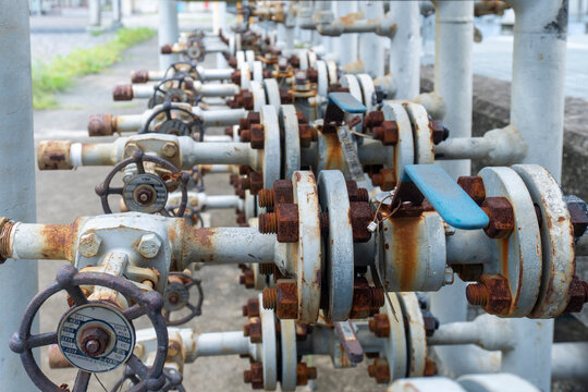 Close-up of a row of heavily rusted industrial gate valves handwheels and flanged pipe fittings creating a repetitive pattern along an aging petrochemical plant pipeline system.