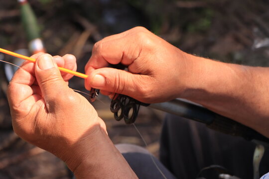 Close-up of a fisherman's hands while assembling and adjusting a fishing rod outdoors.