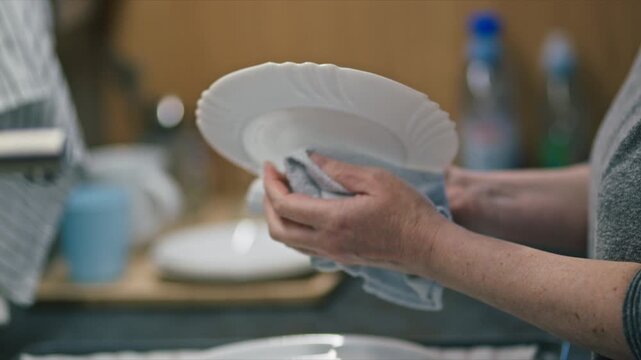 Close-up of hands drying plate with kitchen towel, everyday household routine in warm home setting, 4K