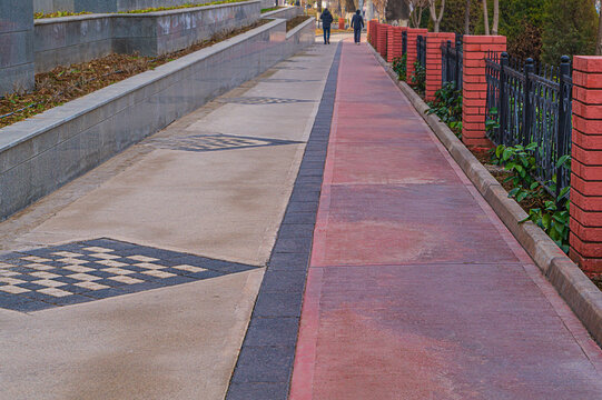 Close-up street strip of pedestrian sidewalk from lower angle with passage of cyclists. Horizontal shot with random two unrecognizable blurred silhouettes of people in the background