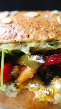 Layered sandwich closeup shows toasted seeded bread, bright vegetables, and creamy filling pressed together. Shallow focus emphasizes moist textures and colorful ingredients for food marketing.