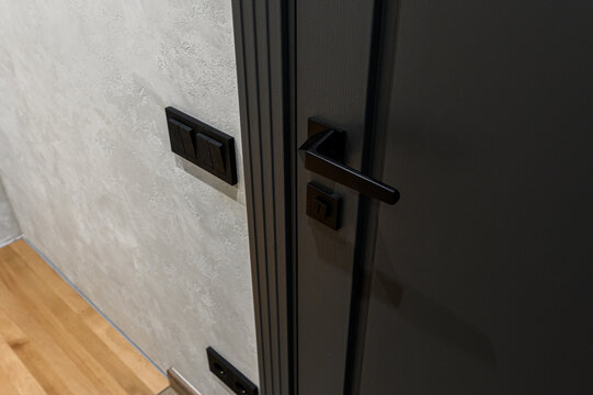 dark‑gray interior door with vertical grooves features sleek black lever handle and matching lock. textured light‑gray wall and wooden floor complete look
