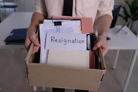 Professional woman carrying cardboard box with resignation letter and office belongings after quitting job