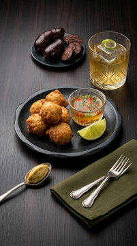 Crispy cod fritters served with sauce, accompanied by a refreshing drink and blood sausage