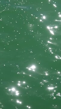 Gr&uuml;n-blaue Wasseroberfl&auml;che eines Sees in Zeitlupe mit glitzernden Lichtreflexen und Schaum, High-Speed-Aufnahme, Hochformat 9:16