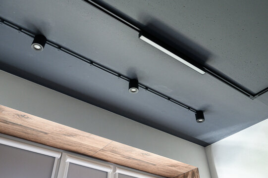 dark ceiling hosts black track rail with cylindrical spotlights and white linear LED fixture. below, wooden trim accents paneled wall.