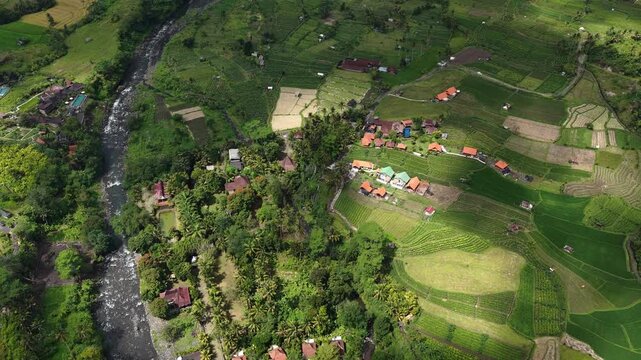 Oblique aerial view of terraced green foothills with winding river and clustered red-roofed houses under soft sunlight, with aerial, river, terrace, agriculture detail