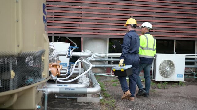Industrial engineer inspecting water valves and pipelines outside a factory using a laptop, supporting infrastructure maintenance, system monitoring, safety, efficient operations and water management.