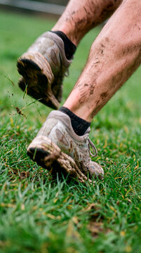 Muddy runner sprints across green grass field during intense trail workout