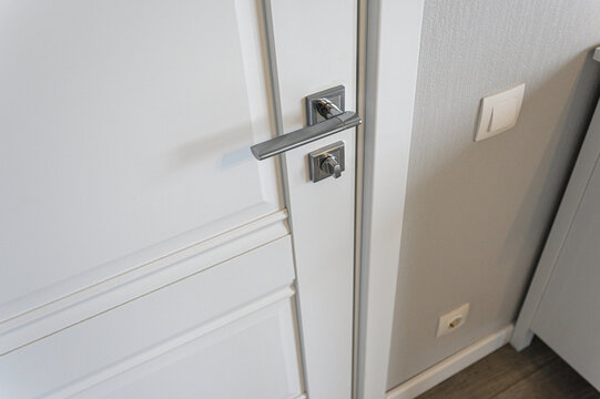 White paneled interior door features sleek brushed‑metal lever handle and matching lock. neutral wall hosts minimalist switch and socket