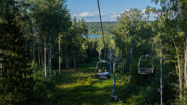 Summer chairlift ride over green forest, couple in a cable car, lake and hills on the horizon.