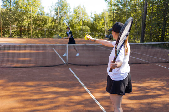 Preparing to serve, tennis player with a ball in her hand against the light, backlit summer game.