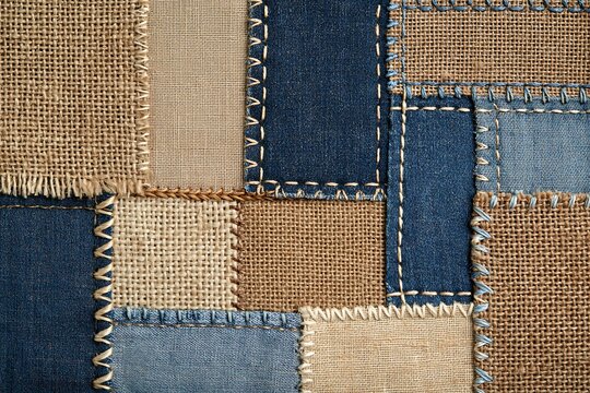 Patchwork background made of various denim and burlap fabric textures stitched together with decorative embroidery thread