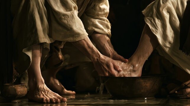 Close up of jesus washing a disciple's feet in a dim setting with strong light and shadow contrast