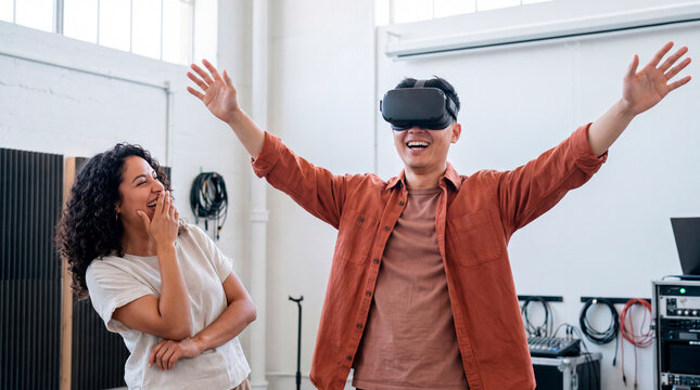 Man wearing VR headset celebrates while woman laughs on sofa nearby indoors