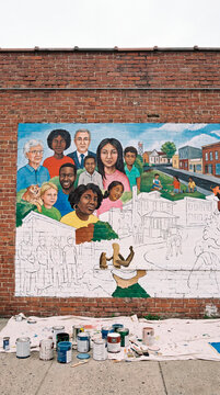 Community mural in progress covers weathered brick wall with paint cans below
