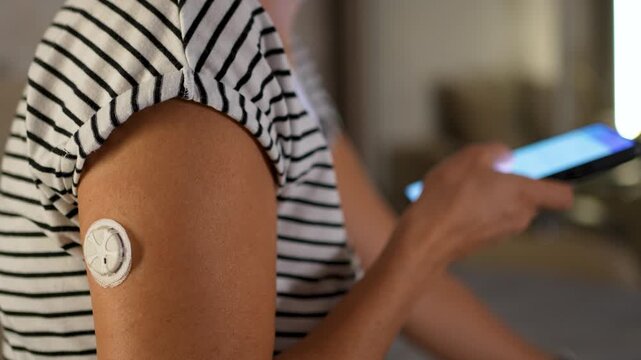 Close-up shot of a woman using a smartphone diabetes app to scan a continuous glucose monitoring (CGM) sensor on her arm