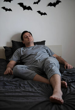 Insomnia and sleep disorder, exhausted man sleeping in bed with halloween bat decorations on wall nightmares and night terrors in bedroom