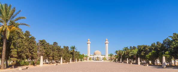 Obraz premium Bright sky highlights historic monument, Majestic mausoleum with twin minarets glows brightly, Peaceful courtyard surrounded by intricate tilework and golden finials in sunlight