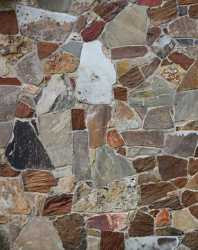 Multi-color machine-cut veneer stone and recessed mortar wall surface with three triangular stones forming a geometric visual arrangement in a vertical composition, with varied natural stone textures