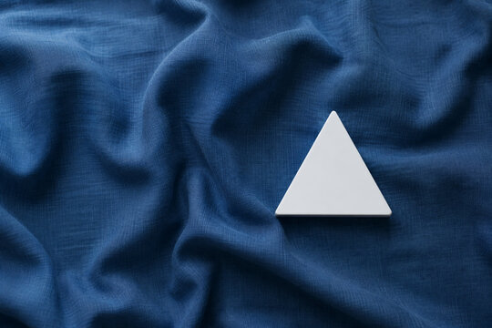 Single white equilateral triangle object on deep blue linen, calm still life for editorial concept