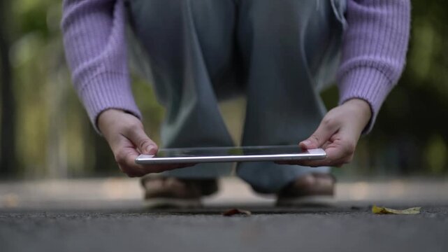 A woman holds a broken tablet with a shattered screen after it was smashed against asphalt, showing technology damage, accident, repair and replacement.