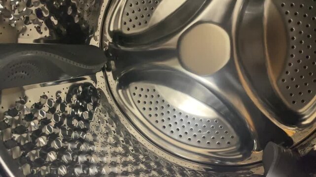 Macro close up view of clean empty stainless steel washing machine drum interior with perforations and lifter horizontal stock video. High quality 4k footage