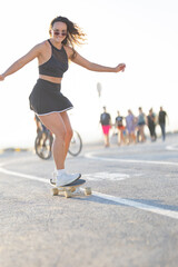 Young woman rides skateboard along boardwalk during daytime with people walking in the background © KONSTANTIN SHISHKIN