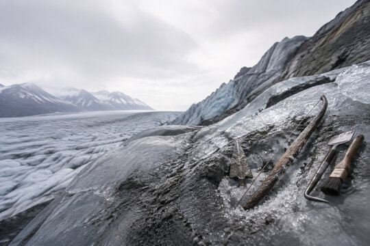 Glacier landscape with small excavation site, ancient bow and arrowhead in ice, archaeological tools