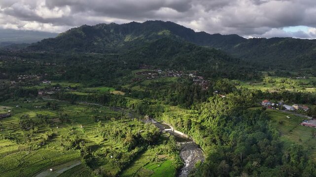 Aerial panorama of tropical foothills with winding river and shifting cloud shadows over Mount Agung, with landscape, foothill, mountain, valley detail, showing river, stream, forest, jungle context
