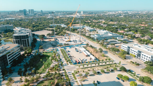Lattice boom crane works active excavation site near Kaleidoscope Park grounds. Lowrise offices border paved lots, reflecting continuous commercial growth across Frisco, Texas