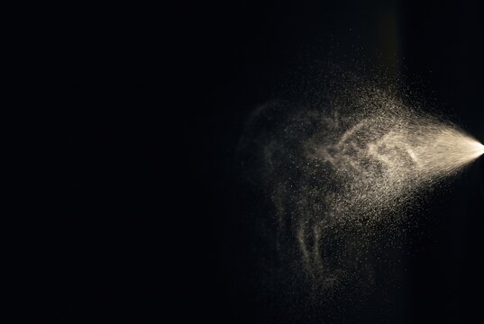 Fine particles scatter in a specific pattern creating a visual effect. The background is dark and empty, allowing for clear focus on the dust