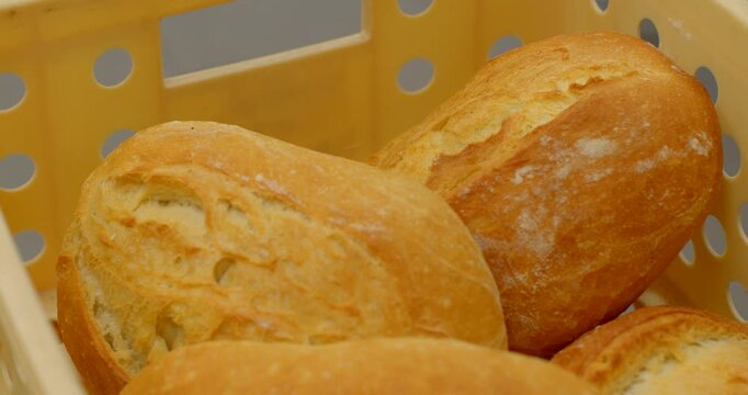 close-up motion scene of multiple freshly baked bread rolls resting inside perforated plastic bakery crate, stationary and ready-for-sale, warm even indoor, with