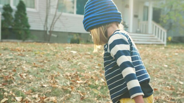 Boy walking across a leaf-scattered autumn lawn while holding a tricycle handle
