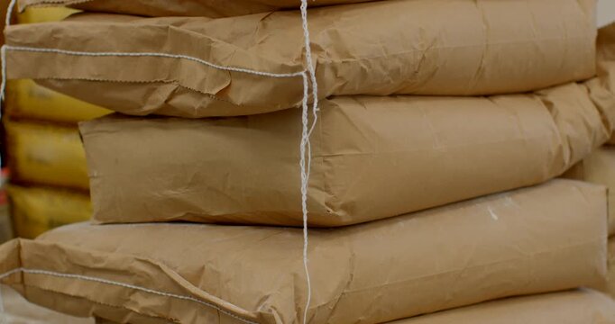 stacked brown kraft paper sacks arranged on worn cardboard pallet in indoor storage area, midsection of stack highlighted with hanging paper twine, compressed sack
